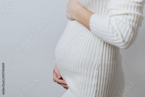 Monochrome portrait of an unrecognizable pregnant Caucasian girl in a knitted dress.