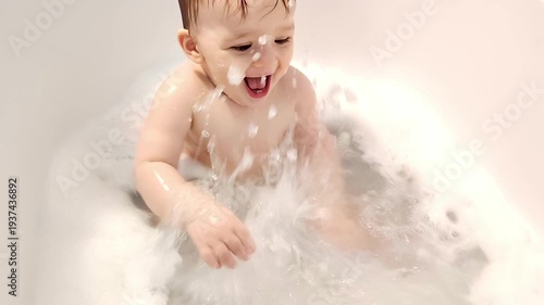 Happy little baby boy splashing water in a bathtub