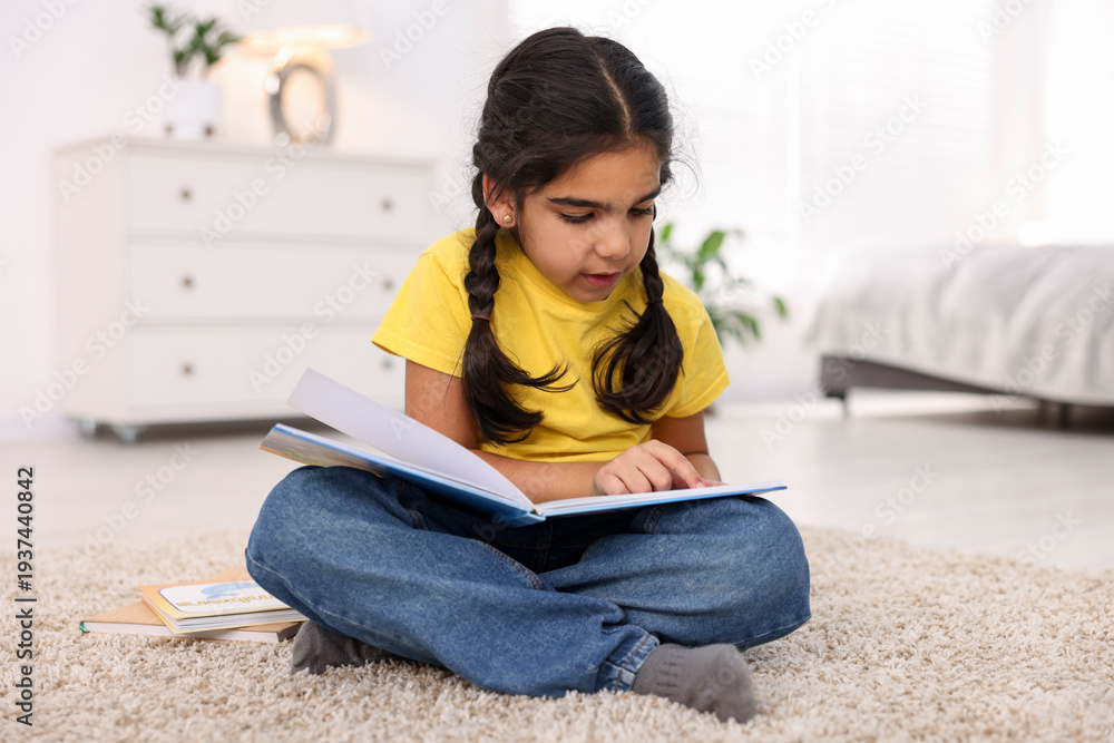 Naklejka premium Cute little girl reading book on floor at home