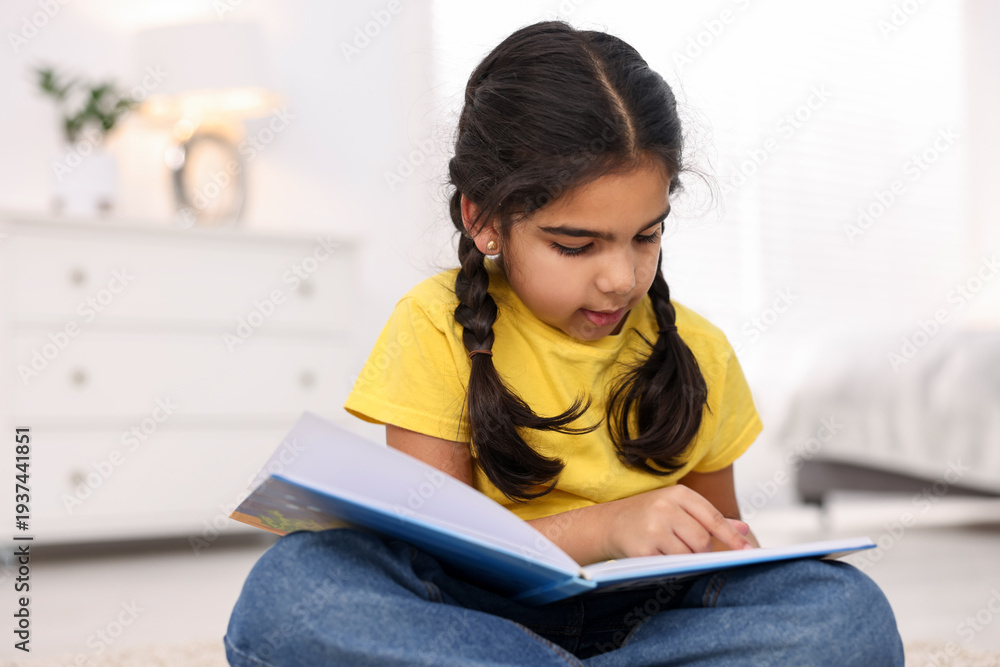 Naklejka premium Cute little girl reading book at home