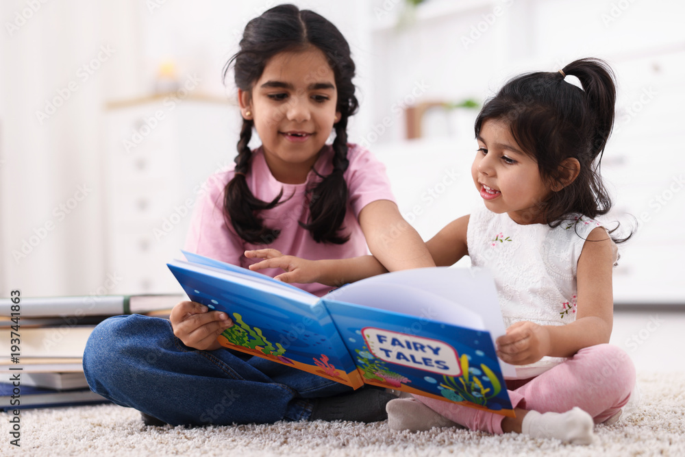 Naklejka premium Cute little girls reading book together at home
