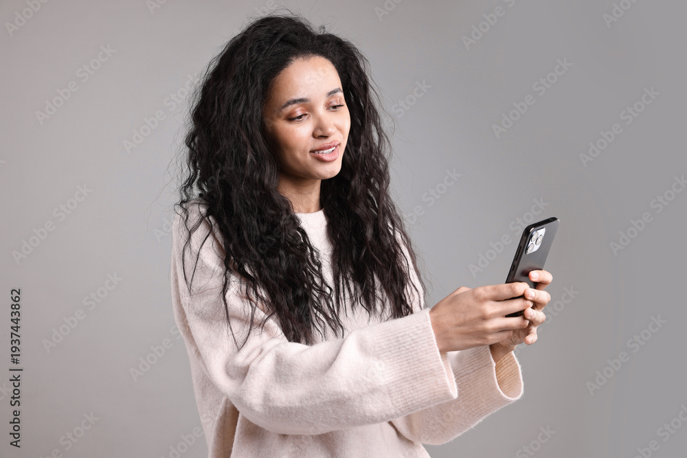 Fototapeta premium Beautiful young woman with smartphone on light grey background