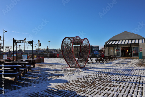 Skegness Pier and Heart of Skegness sculpture surrounded by winter snow; frosty seaside scene on Lincolnshire Coast with rare snowfall seen along historic Victorian Pleasure Pier, Lincolnshire, UK