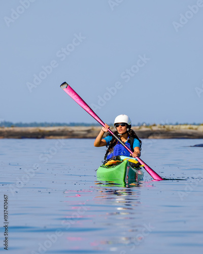 Foto Front view of a female kayaker in a green boat using a pink paddle and wearing a safety helmet and life jacket