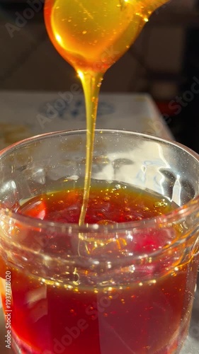 A close-up shot of honey being poured into a glass jar with a clear golden texture. Perfect for food and cooking content, showcasing honey pouring action.
