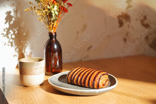 Cozy coffee shop ambiance with a latte and dried flowers in a brown bottle on a wooden table