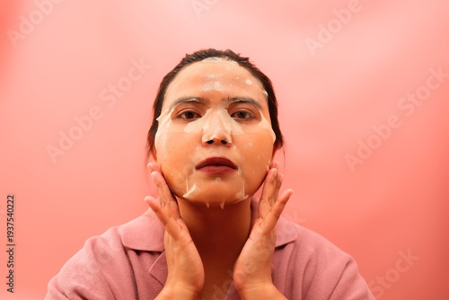 Beautiful Asian woman applying a sheet mask for facial hydration and skincare treatment.