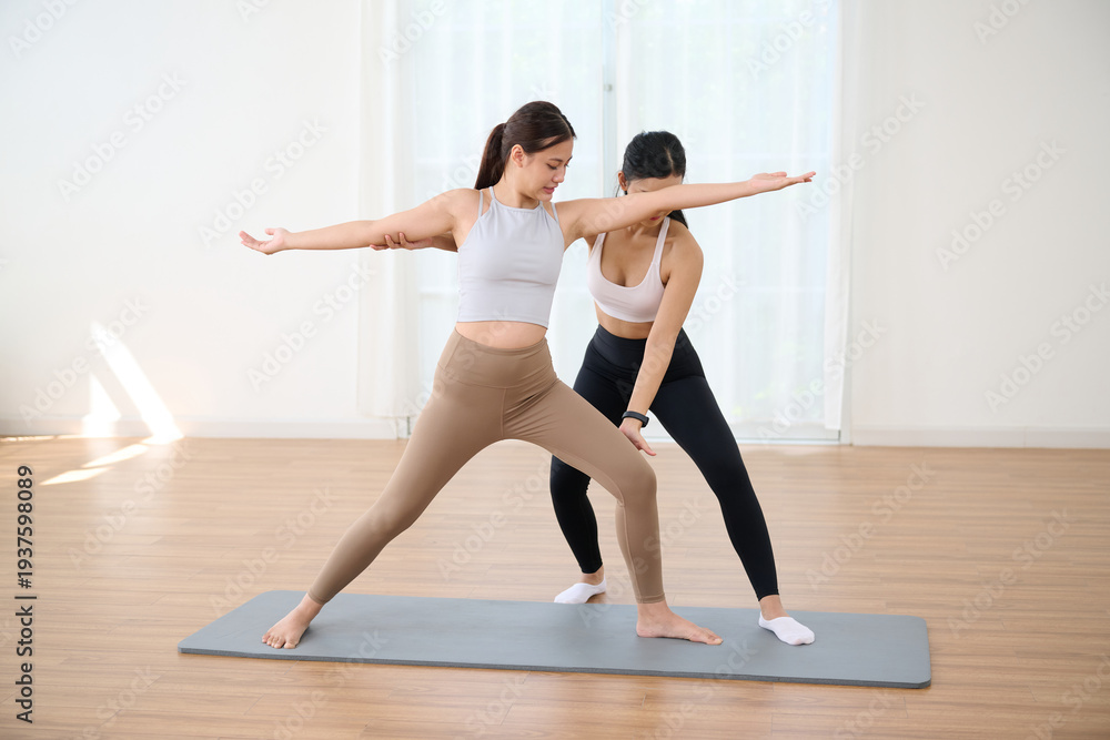 Fototapeta premium Women practicing yoga together with arms outstretched for balance, helping and supporting each other