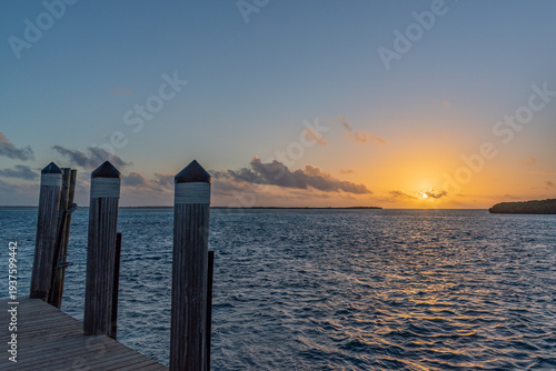 Orange sunrise over boat dock and calm tropical ocean