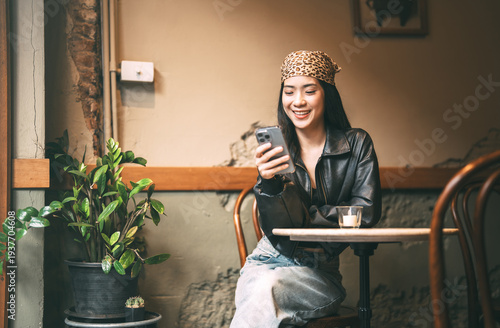 Young adult happy asian woman using mobile phone for social media application hipster fashion style with bandana urban vibes