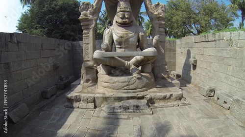 Drone shot rising from Narasimha statue to palms and sky in Hampi India.