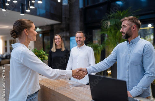 Young business people shaking hands in modern lobby or reception area with colleagues watching