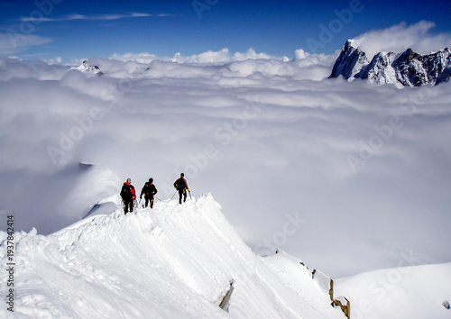 Three climbers ascend a snowy mountain ridge above a sea of clouds, braving the elements for the summit.
