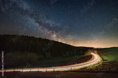 Winding road illuminated by car light trails under a brilliant starry night sky showcasing the milky way galaxy.