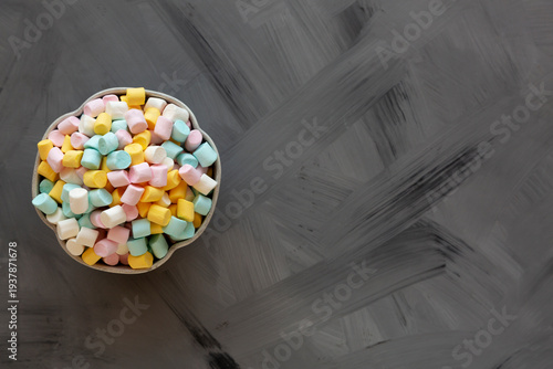 Unhealthy multi-colored mini marshmallows in a bowl, top view. Space for text.