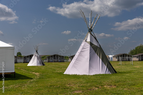 Beautiful view of few summer camping tipi in field. Tee pee built on green grass. Traditional teepee tent wigwam located in nature