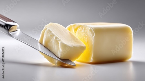 A knife slicing a fresh block of creamy butter on a clean white surface