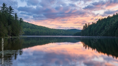 Serene lake reflecting a colorful sunset surrounded by lush green forests and cloudy skies