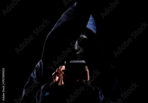 Canvas Print A scammer, hiding his face under a black mask, uses a telephone to make calls to deceive people in a dark room