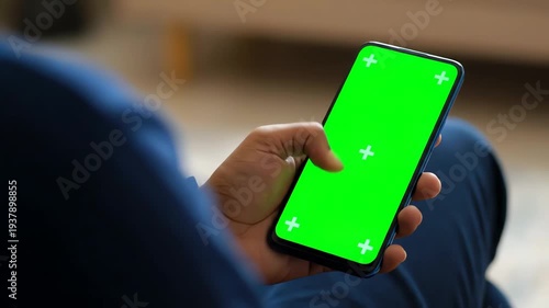 Person Holding Phone with Green Screen in Blue Attire Indoors Finger Touching Screen for Interactive Interface Modern Technology Concept