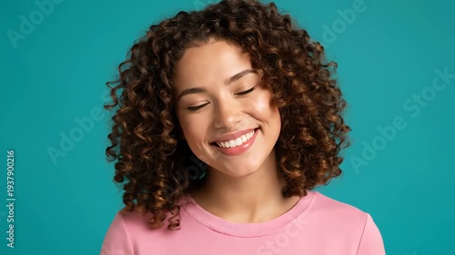 Smiling Woman with Curly Hair and Pink Shirt Posing Against Teal Background in Studio Lighting