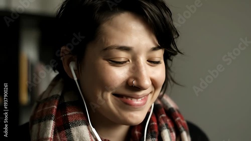 Smiling Young Woman with Earphones and Plaid Scarf Against a Neutral Background with Soft Natural Lighting