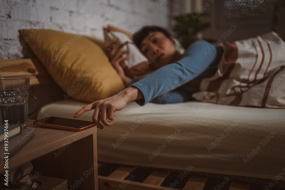 Obraz premium Woman waking up reaching for smart phone alarm