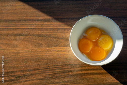 Raw egg yolks in white bowl on wooden table