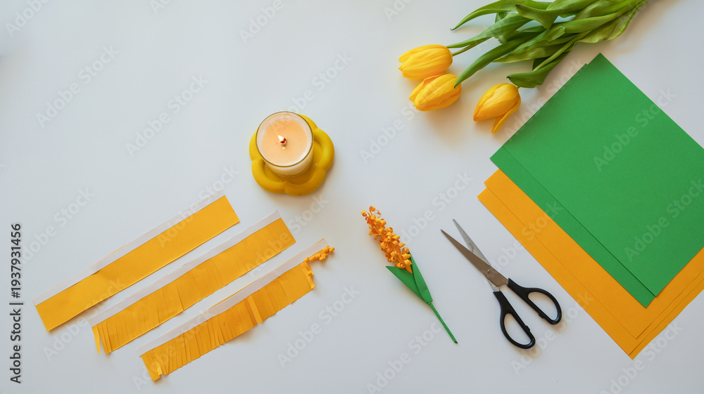 Naklejka premium DIY spring craft project with yellow tulips, paper, scissors, and a lit candle