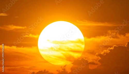 A bright sun sets behind dark orange clouds in the sky