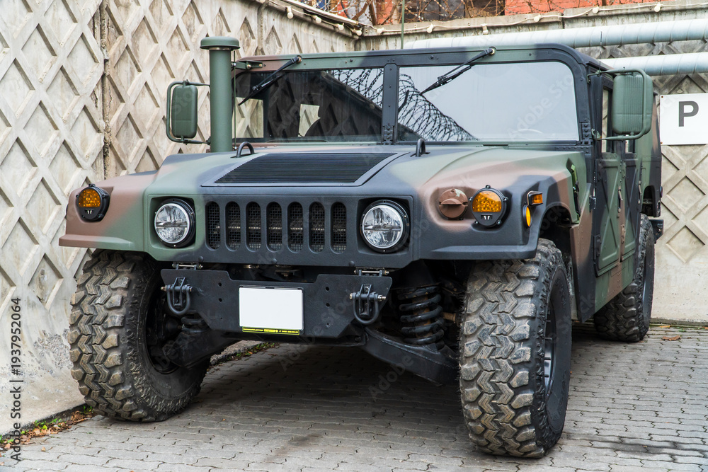 Naklejka premium Military Humvee parked on an street, showcasing its rugged design and operational readiness in a secure military base. Khaki camouflage military Hummer front view. HMMWV.