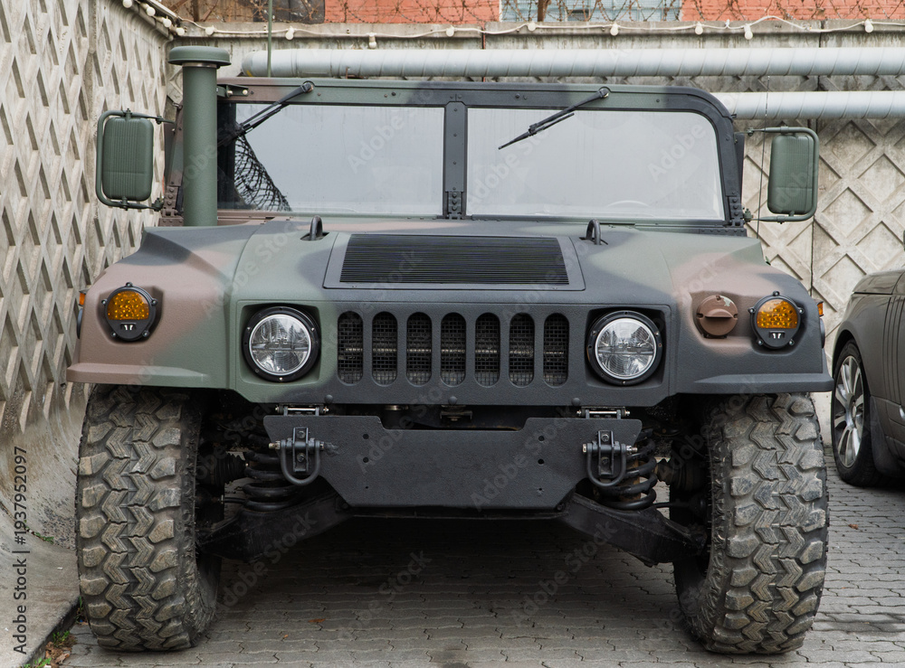 Fototapeta premium Military Humvee parked on an street, showcasing its rugged design and operational readiness in a secure military base. Khaki camouflage military Hummer front view. HMMWV.