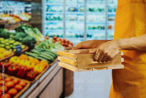 Supermarket worker holding wooden crate near fresh produce