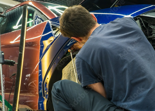 Process of paintless dent repair on car body. The mechanic at the auto shop with tools to repair dents in car body. Body repair. PDR. A specialist repairs a dent on the car body without painting.