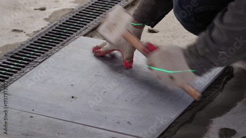 Professional builder worker installing floor a large ceramic tile at repair renovation work using a laser level. Man experienced repairman laying placing tile indoors house or apartment. Worker. 