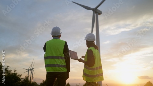 Foto Engineers with hard hats and high visibility vests inspecting a wind farm at sun
