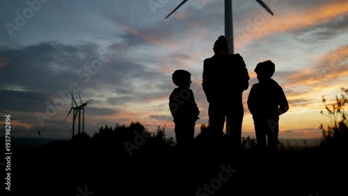 Εκτύπωση καμβά Family watching sunset over wind farm, silhouettes of a mother and her children