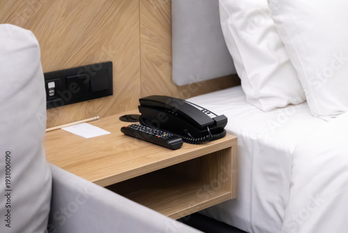 Modern hotel room bedside table features a black telephone, TV remote, and convenient USB charging ports, highlighting guest comfort and essential amenities