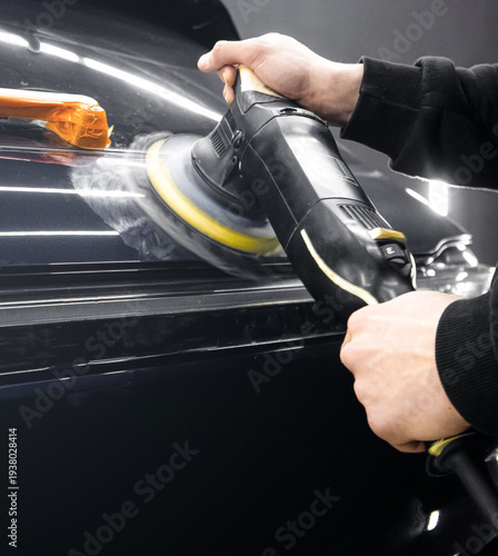Concept car detailing. Male hands with orbital polisher in auto repair shop. Hands with an orbital polishing machine in an auto repair shop. Car detailing on-site service man polishing a black car. 