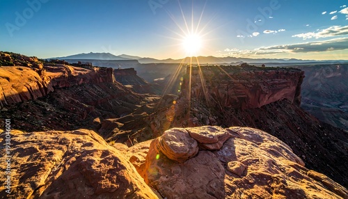 Sun bursts above canyon, illuminating rocky landscape with orange glow on a clear day