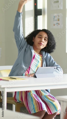 Vertical video: Teacher cueing student in striped dress raising hand at school with tablet to speak