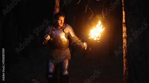 A knight in full armor, his face bloodied and scarred, holding a sword and torch, is sneaking through a dark night forest. A medieval warrior searches in the darkness.