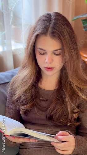 Beautiful young happy woman reading a book at home lying on the sofa