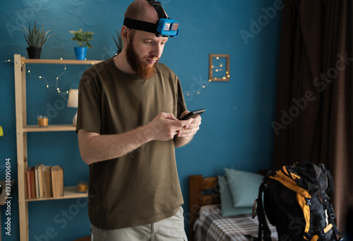 Bearded male hiker setting action camera for travel vlog preparing to travel journey at home interior