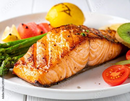 A grilled salmon fillet with vegetables and lemon on a white plate