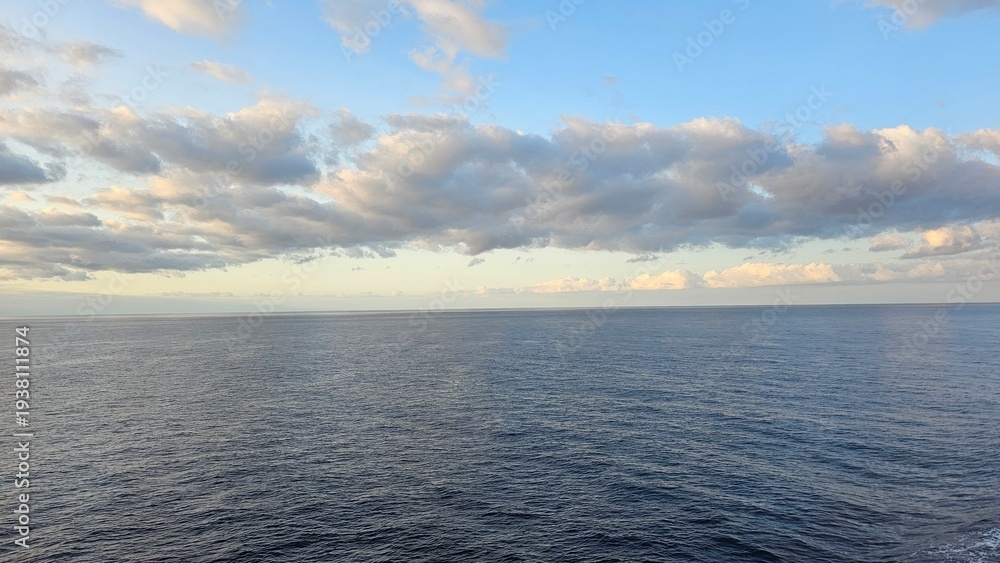 Obraz premium Wide open view of the Atlantic Ocean near Madeira Island with calm blue water and a dramatic cloud-filled sky stretching across the horizon during soft evening light.