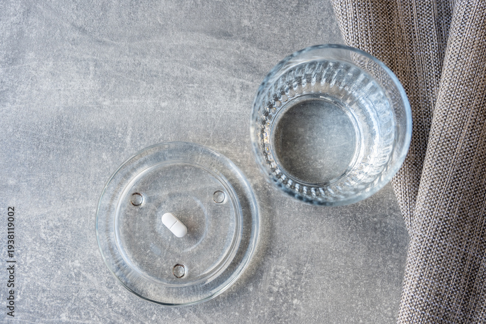 Obraz premium White pill and glass with water stay on the marble table.