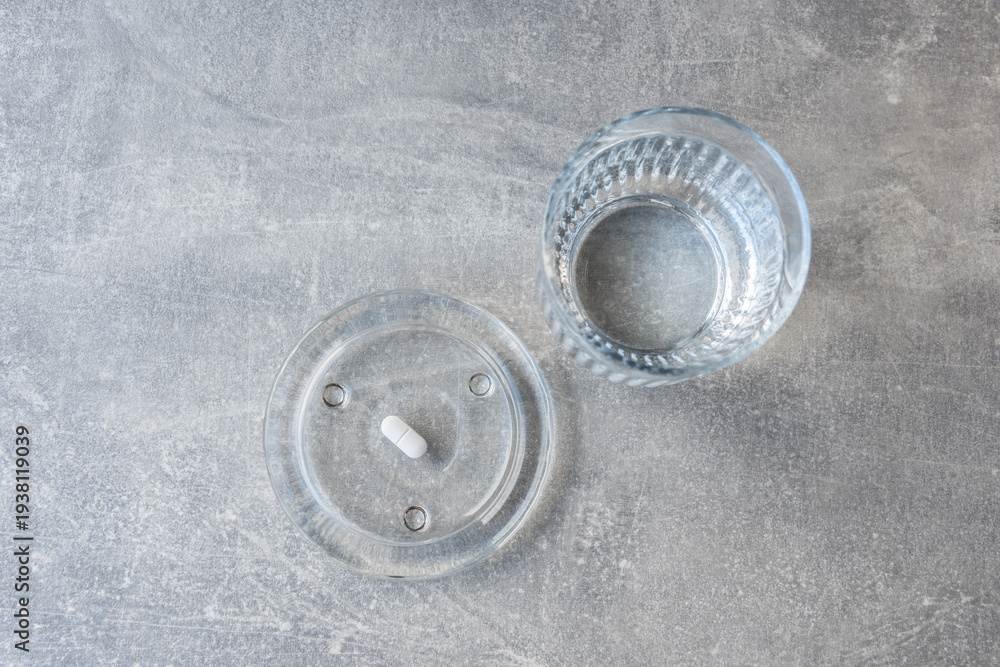 Obraz premium White pill and glass with water stay on the marble table.