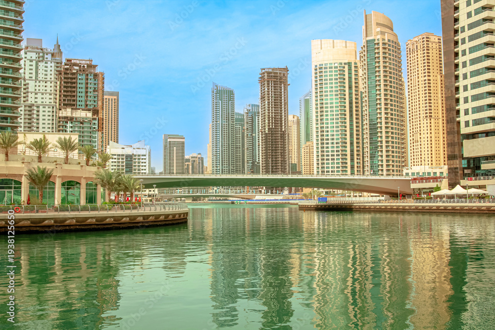 Obraz premium Dubai Marina skyscrapers creating a modern skyline, reflecting in the tranquil waters of the canal with a bridge connecting parts of the vibrant urban landscape in United Arab Emirates