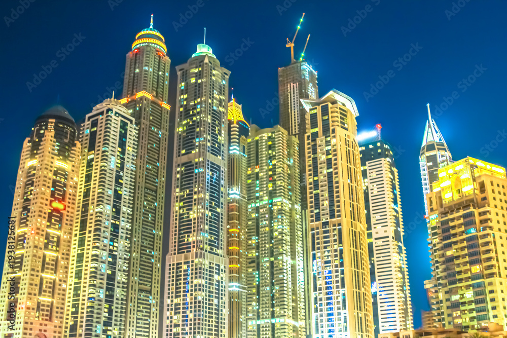 Obraz premium Illuminating Dubai Marina skyline at night, vibrant high-rise towers and glowing lights reflect modern luxury, urban growth and dynamic waterfront architecture in United Arab Emirates